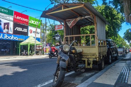 Téléchargez les photos : Une moto pick-up à trois roues ou communément appelée tossa garée sur le côté d'une route urbaine avec un panneau d'affichage en arrière-plan contenant diverses publicités, Indonésie, 17 septembre 2023. - en image libre de droit