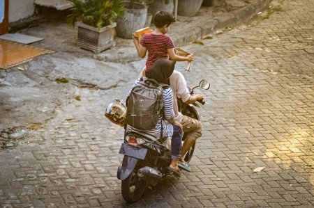 Foto de Una familia formada tanto por padres como por niños que viajan en moto. Su hijo fue visto de pie en el asiento de la moto, Indonesia, 19 de octubre de 2023. - Imagen libre de derechos
