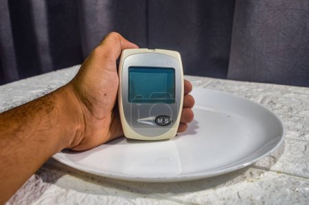 Photo for Hand holding a test tool for blood glucose, cholesterol and uric acid levels on a dinner plate - Royalty Free Image