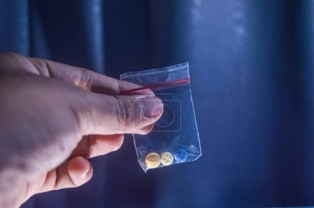 Finger mit drei Pillen für Schizophrene in einem Plastikclip auf dunklem Hintergrund