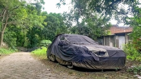 an old car covered in a cover abandoned on the side of the road near the forest