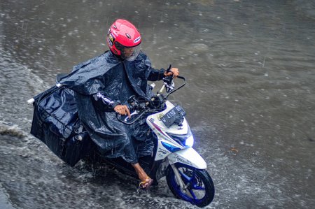 Foto de Un mensajero paquete que monta una motocicleta que conduce a través de las aguas de inundación durante las fuertes lluvias en una zona residencial, Indonesia, 8 de diciembre de 2023. - Imagen libre de derechos