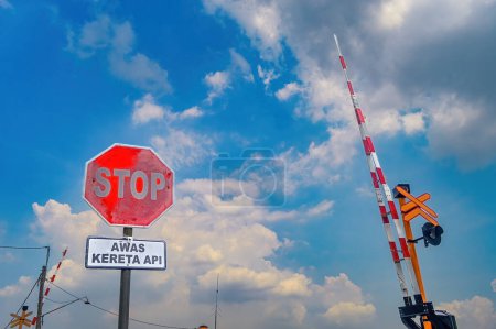 Téléchargez les photos : Un ensemble de panneaux d'arrêt et de barrières aux passages à niveau en Indonésie. Traduction sur le texte du panneau "attention aux trains". - en image libre de droit