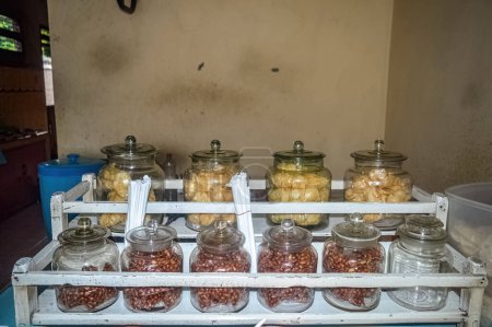Téléchargez les photos : De nombreux bocaux en verre remplis de craquelins et de noix servis dans un simple étal de nourriture indonésien - en image libre de droit