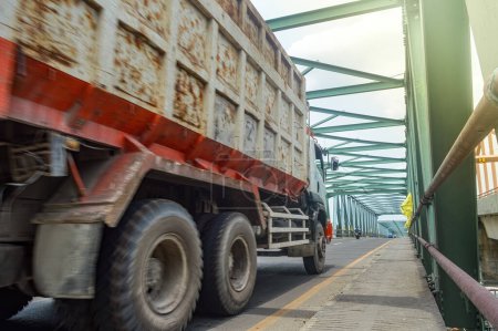 An Isuzu Giga dump truck passes a long steel truss bridge
