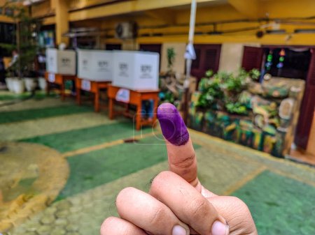 tinta en el dedo índice después de las elecciones presidenciales de Indonesia con el lugar de las elecciones en segundo plano