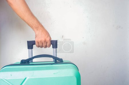la mano de un hombre tirando de una maleta verde turquesa