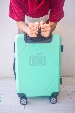 Frustrierter Mann lehnt an einem türkisfarbenen Koffer