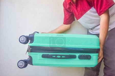 Téléchargez les photos : Un homme mûr a soulevé une valise verte turquoise - en image libre de droit