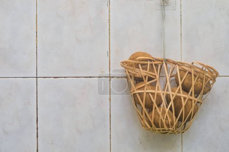 un panier rempli de pommes de terre suspendues à un mur en céramique avec espace de copie