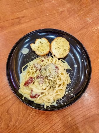 ein Teller Spaghetti Carbonara mit zwei Scheiben Knoblauchbrot auf dem Tisch. Geeignet für italienische Speisekarten