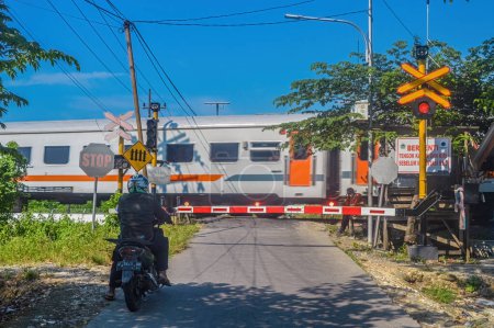Photo for The train crossing was closed because an economy train was passing by. The motorcyclist seemed to stop and wait, Indonesia, 4 May 2024. - Royalty Free Image