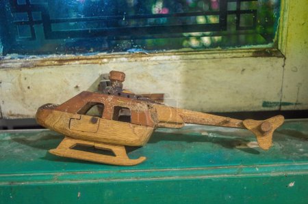 a broken toy or craft helicopter made of wood on the edge of a wooden window frame