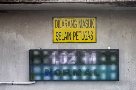 The LED screen contains information indicating the water level of the Bengawan Solo River to prevent flooding in the rainy season. Translation "No entry except officers"