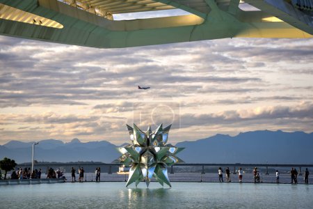 Téléchargez les photos : Un avion survolant la sculpture Puffed Star II à la surface de l'eau du musée de demain - Rio de Janeiro, Brésil - en image libre de droit