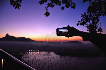 Téléchargez les photos : Photographier la baie de Guanabara et la montagne Corcovado avec un téléphone portable depuis le pain de sucre au crépuscule - Rio de Janeiro, Brésil - en image libre de droit