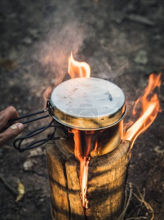 Photo for Water boiling in a metal pot on Swedish Fire Log. Burning a Swedish candle, swedish torch in summer evening in a forest with fire and smoke - Royalty Free Image