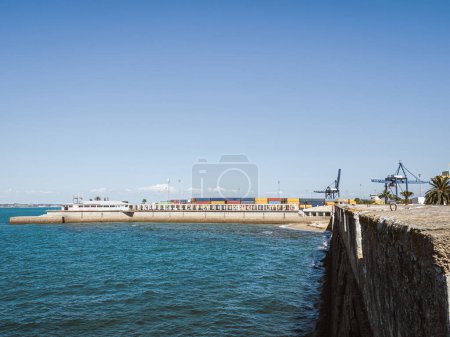 Blick auf den Frachthafen von Cadiz, Spanien, mit bunten Containern, Kränen und Palmen am Meer, Sommer