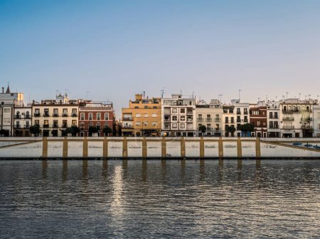 Colorful buildings including homes and shops face the Guadalquivir River in the Triana District of the Analusian city of Seville, Spain during golden hour summer sunset