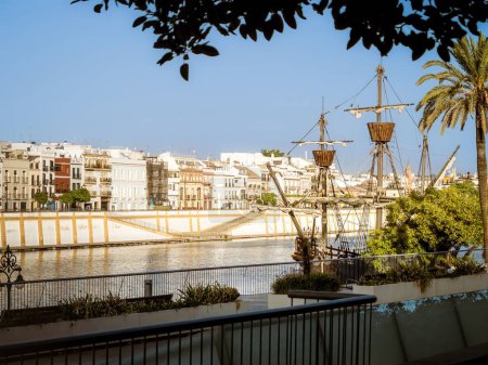 Le Nao Victoria réplique carrack navire amarré à la rivière Guadalquivir en face des maisons du quartier de Triana de Séville, Espagne, coucher de soleil heure dorée