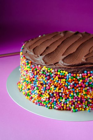Delicioso pastel de cumpleaños de ganache de chocolate con espolvoreos de colores sobre un fondo rosa