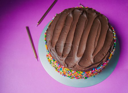 Photo for Delicious chocolate ganache birthday cake with colorful sprinkles on a pink background - Royalty Free Image