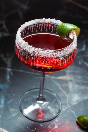 Red alcoholic cocktail, lime garnish, salted rim, marble background, ornate glass, fairy lights