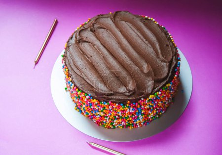 Delicioso pastel de cumpleaños de ganache de chocolate con espolvoreos de colores sobre un fondo rosa