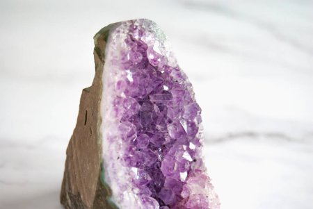 Foto de Primeros planos de geoda amatista cruda púrpura oscura, fondo de mármol blanco, piedra semipreciosa - Imagen libre de derechos