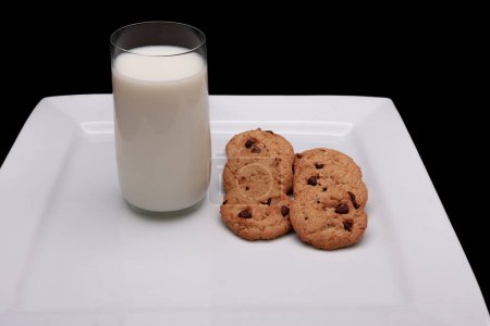 Foto de Un vaso de leche y media docena de galletas en un plato sobre un fondo negro - Imagen libre de derechos