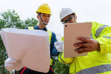 Téléchargez les photos : Ingénieur discutant des détails de la route sur le chantier, tenant des plans et un ordinateur portable - en image libre de droit