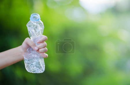 Hand squeezing a plastic bottle on a green background. It represents the movement against pollution and recycling.