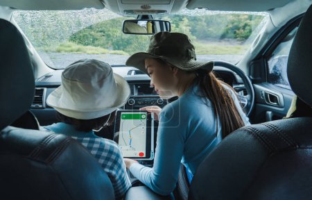 Photo for An Asian mother and daughter plan a trip in their car using an online satellite navigation system on a large tablet screen. - Royalty Free Image