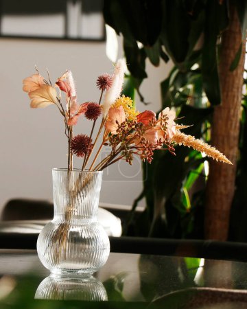 schöne trockene Blumen mit Vase auf einem Glastisch