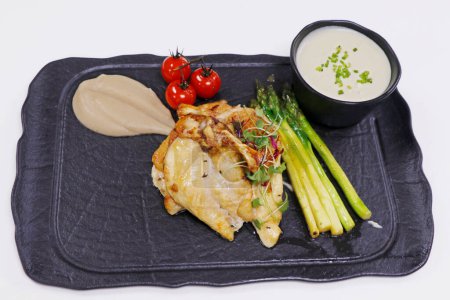 Téléchargez les photos : Poitrine de poulet nourrie au maïs avec purée de pommes de terre, asperges et tomates cerises dans une assiette noire - en image libre de droit