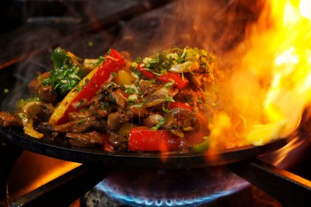 Photo for Mexican food smoking chicken and beef fajitas on sizzling plate with fire and smoke - Royalty Free Image
