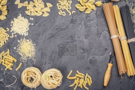 Photo for Pasta month. Assortment of uncooked pasta and noodles over black stone background, top view with copy space for text. Italian food culinary concept. Collection of different raw pasta on cooking table - Royalty Free Image