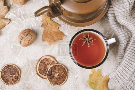 Foto de La bebida otoñal - el té caliente en la taza de esmalte. Fondo otoñal con hojas secas, frutos secos, suéter de punto y especias - Imagen libre de derechos