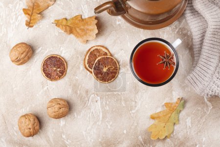Foto de La bebida otoñal - el té caliente en la taza de esmalte. Fondo otoñal con hojas secas, frutos secos, suéter de punto y especias - Imagen libre de derechos