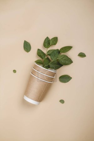 Téléchargez les photos : Tasses à café en papier et feuilles de plantes. Concept écologique, fond d'emballage zéro déchet - en image libre de droit