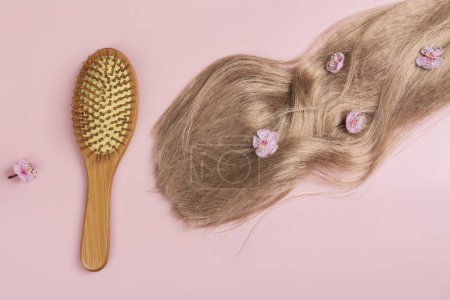 Photo for Long blond hair with sakura flowers and bamboo hair brush on pink background. International Hair Day. Bad Hair Day. Copy space - Royalty Free Image