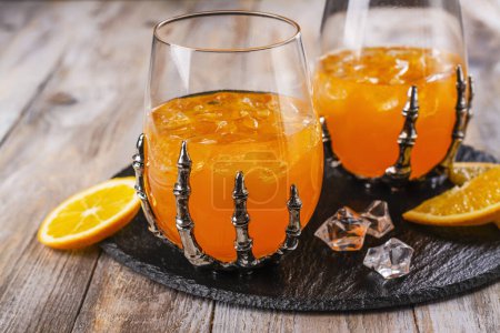 Photo for Halloween orange cocktail in spooky skeletons hand glasses - Royalty Free Image