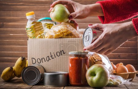 Photo for Woman filling in food donation box. Pasta, cereals, various canned food in a carboard box. National food bank day or food delivery background - Royalty Free Image