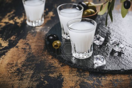Foto de Vodka ouzo griego tradicional y aceitunas marinadas sobre mesa de madera rústica - Imagen libre de derechos
