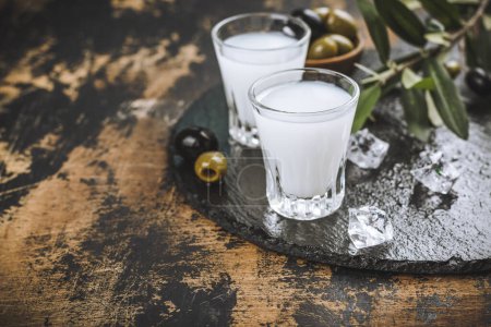 Téléchargez les photos : Vodka traditionnelle grecque ouzo et olives marinées sur table rustique en bois - en image libre de droit
