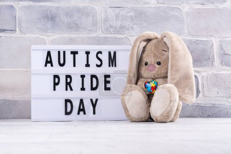 Téléchargez les photos : Jour de la fierté autiste - 18 juin. Journée mondiale de sensibilisation à l'autisme ou fond mois. Jouet de lapin mignon avec coeur de puzzle dans les pattes Copier l'espace - en image libre de droit