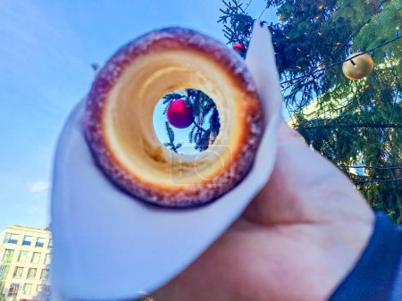 Man holds in hand Trdlo or Trdelnik, Traditional tasty baked Czech Republic a Christmas tree in the background. High quality photo