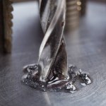metal drill bit with lubrication oil liquid make holes in steel billet on industrial drilling machine. Metal work industry