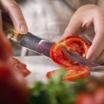 Chef slicing tomato using knife on the table in restaurant. Process of cutting and preparation food in kitchen.