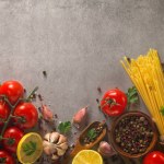 Italian food background on stone table. Macaroni, basil and vegetables.